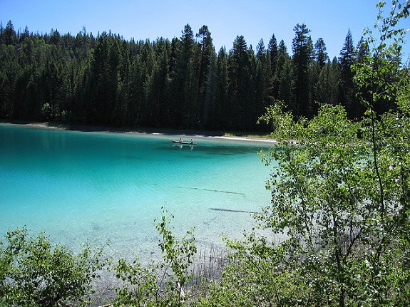 A couple canoes on a peaceful turquoise lake, surrounded by trees.