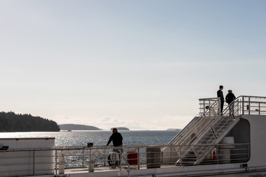 Passengers enjoy the view from the deck looking out at the ocean and across to the island as the ferry crosses the ocean.