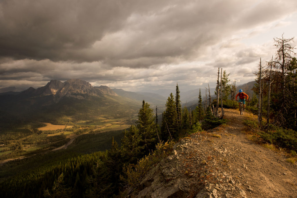 Mountain biking on a path that overlooks a deep valley under a cloudy sky.