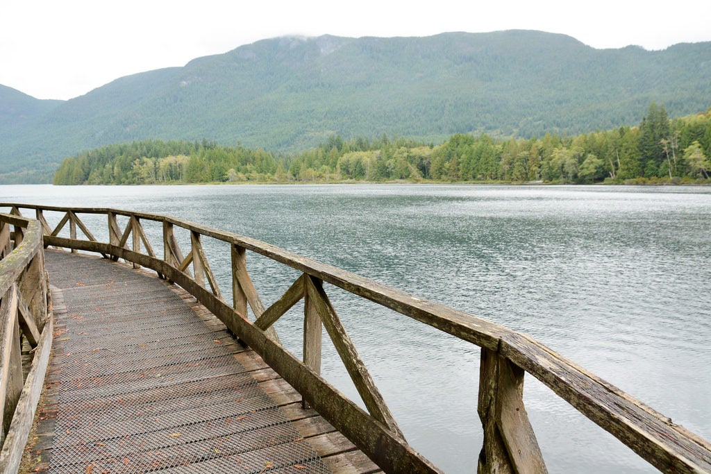 A wooden boardwalk takes you past the ocean and a green mountain range.