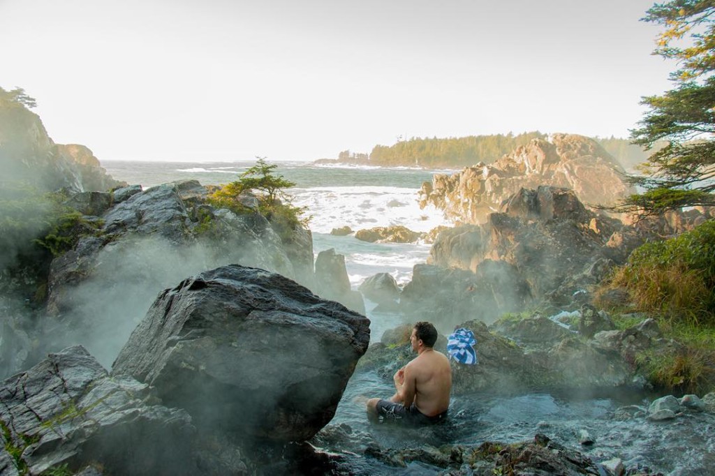 A man in swim trunks sits in a hot springs pool.