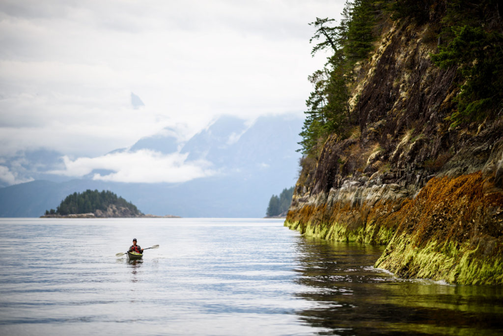 A kayaker paddles along a rocky coastline.