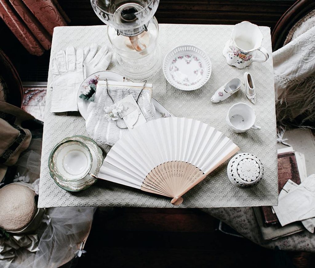 A beautiful table setting of china tea cups, saucers, white gloves, and a fan.