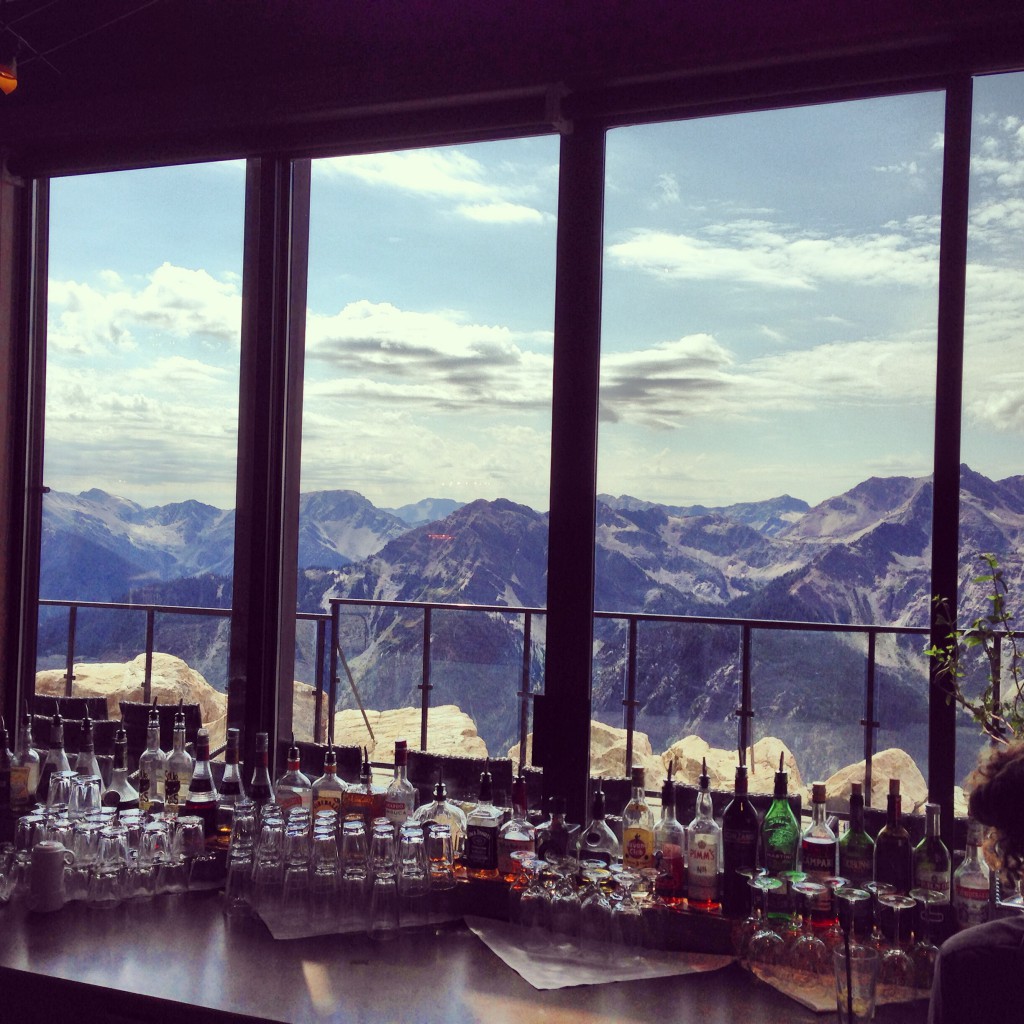 Bottles of liquor and clean glassware sit on a windowsill that overlooks a vast mountain range.