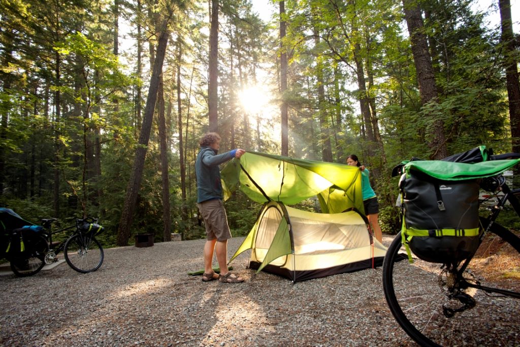 A man and woman pitch their tent in a small clearing in the forest.