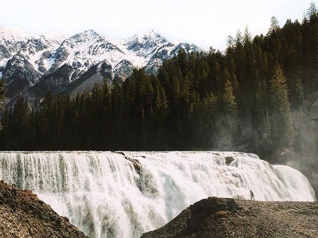 Snow-capped mountains overlook a sprawling waterfall.