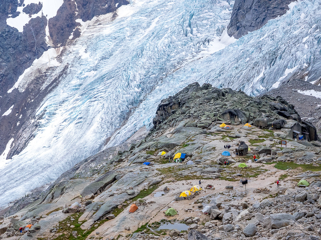 A campground perched on a rocky landscape overlooks a massive glacier.