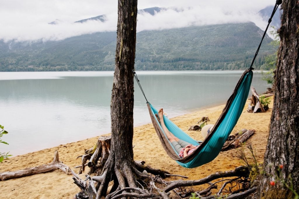 A woman relaxed in a hammock on a beach surrounded by mountains.