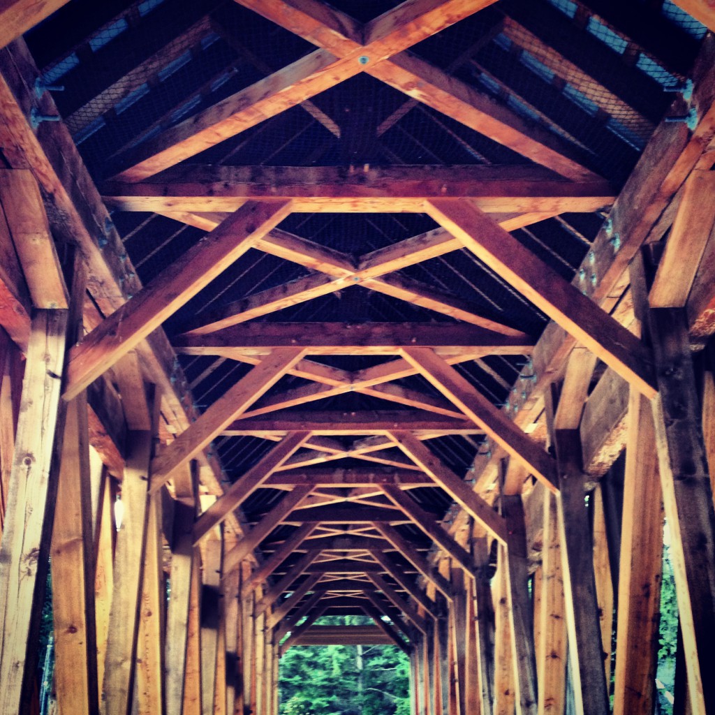 Wooden arches criss cross on the ceiling of a pedestrian bridge.