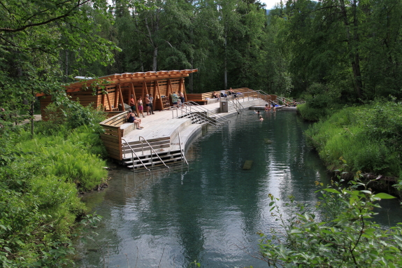 A large outdoor deck sits at the edge of a hot spring in the forest.