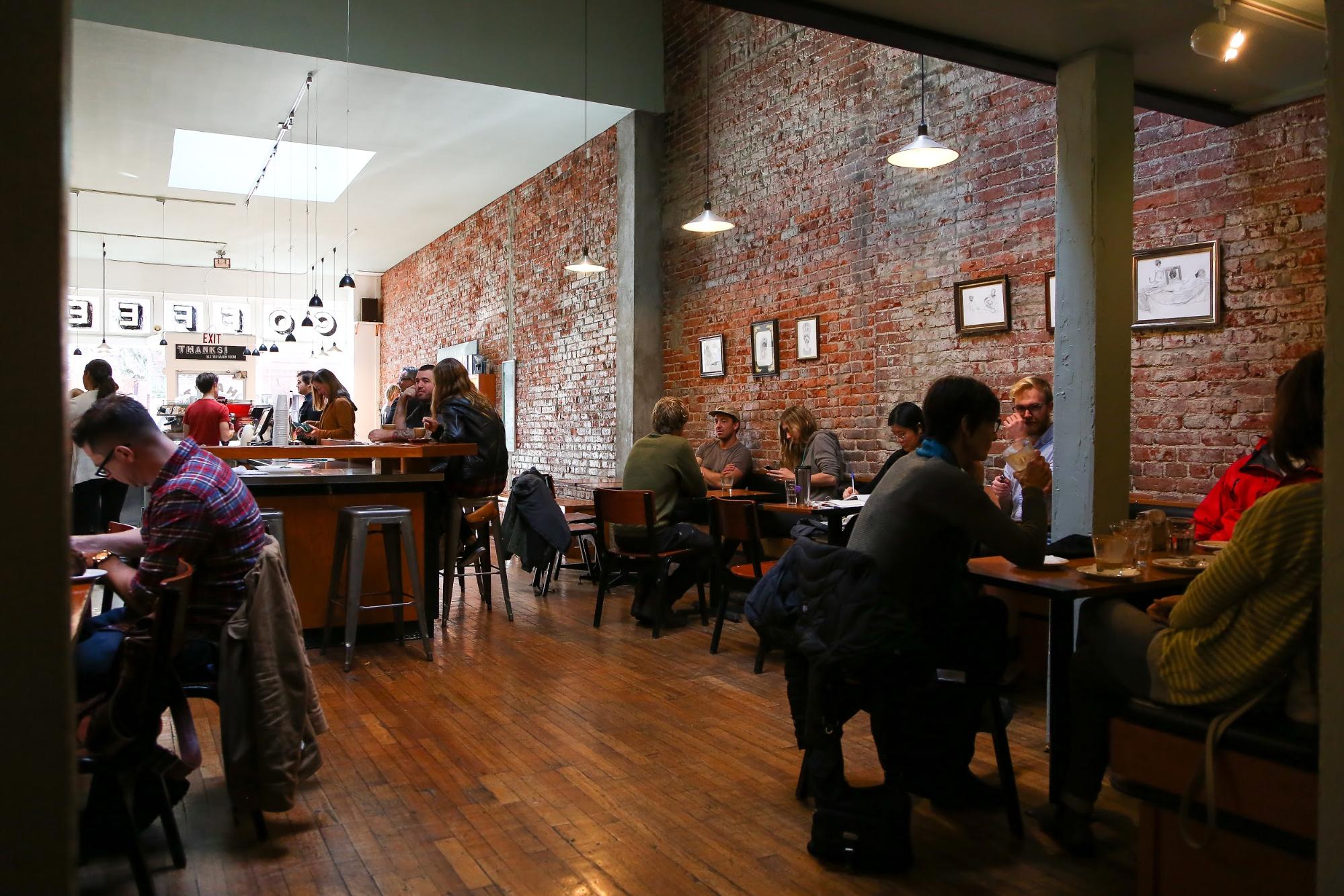Diners sit in a modern coffee shop with brick walls.