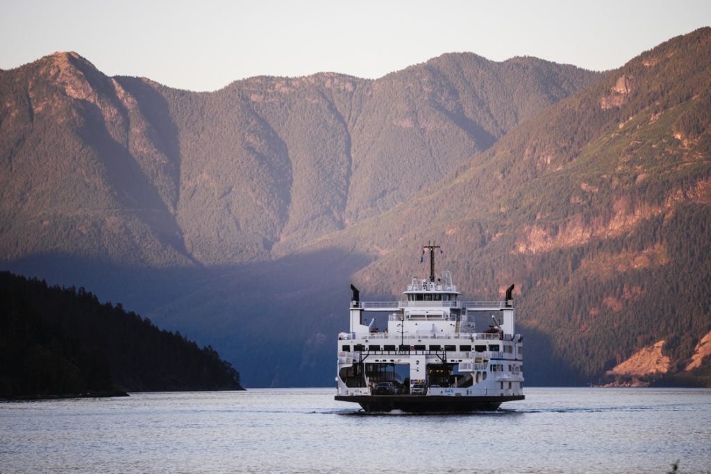 A BC Ferry on the water as the sunsets over the mountains