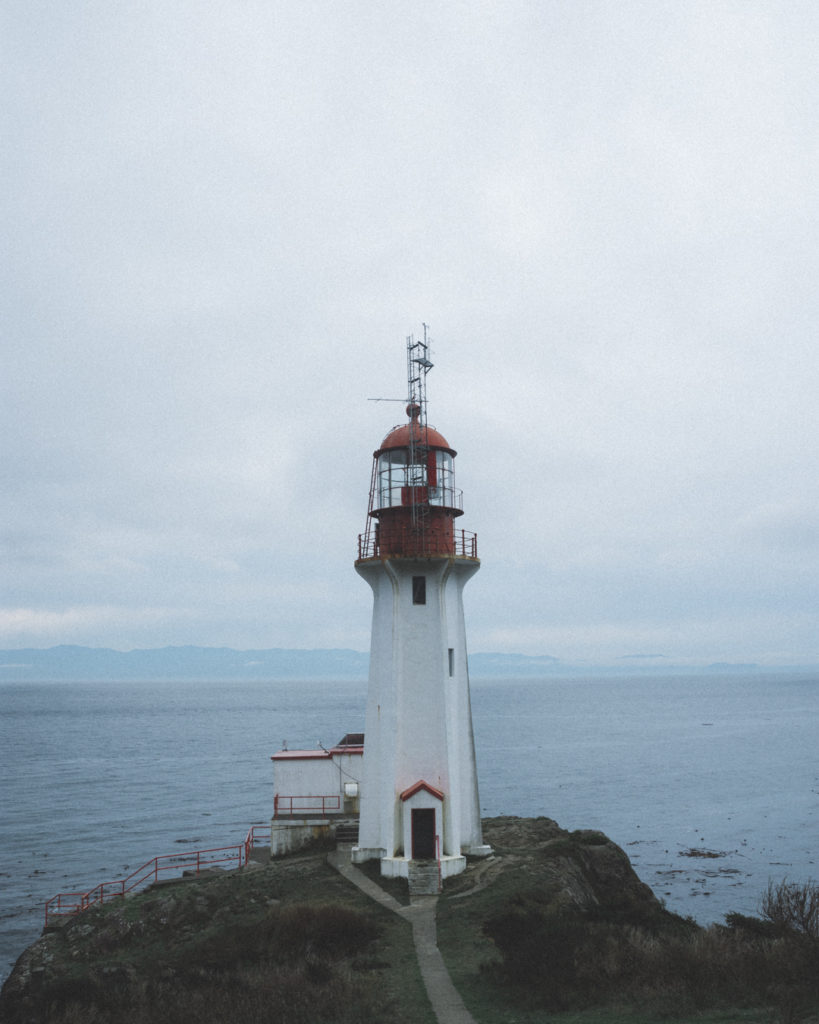 A lighthouse sits at the edge of the ocean under an overcast sky.