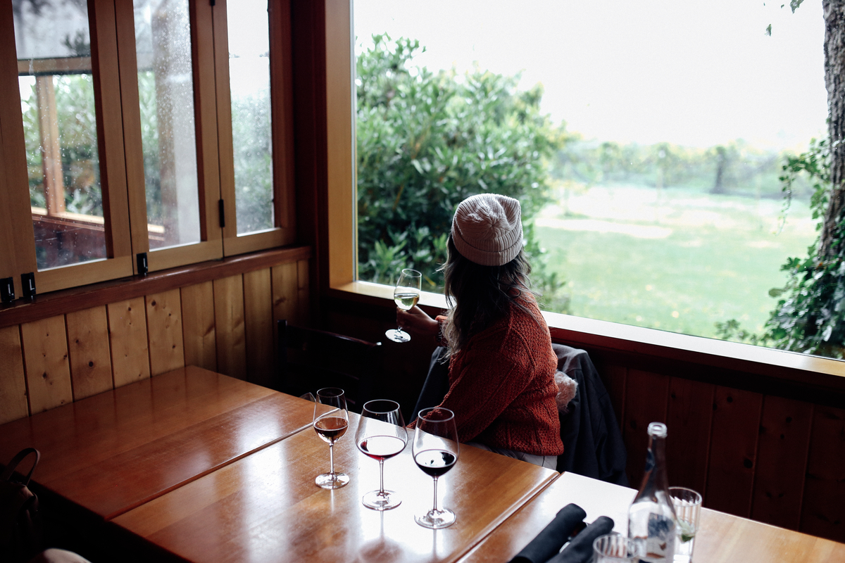 A women sits inside and looks out through an open window at a vineyard