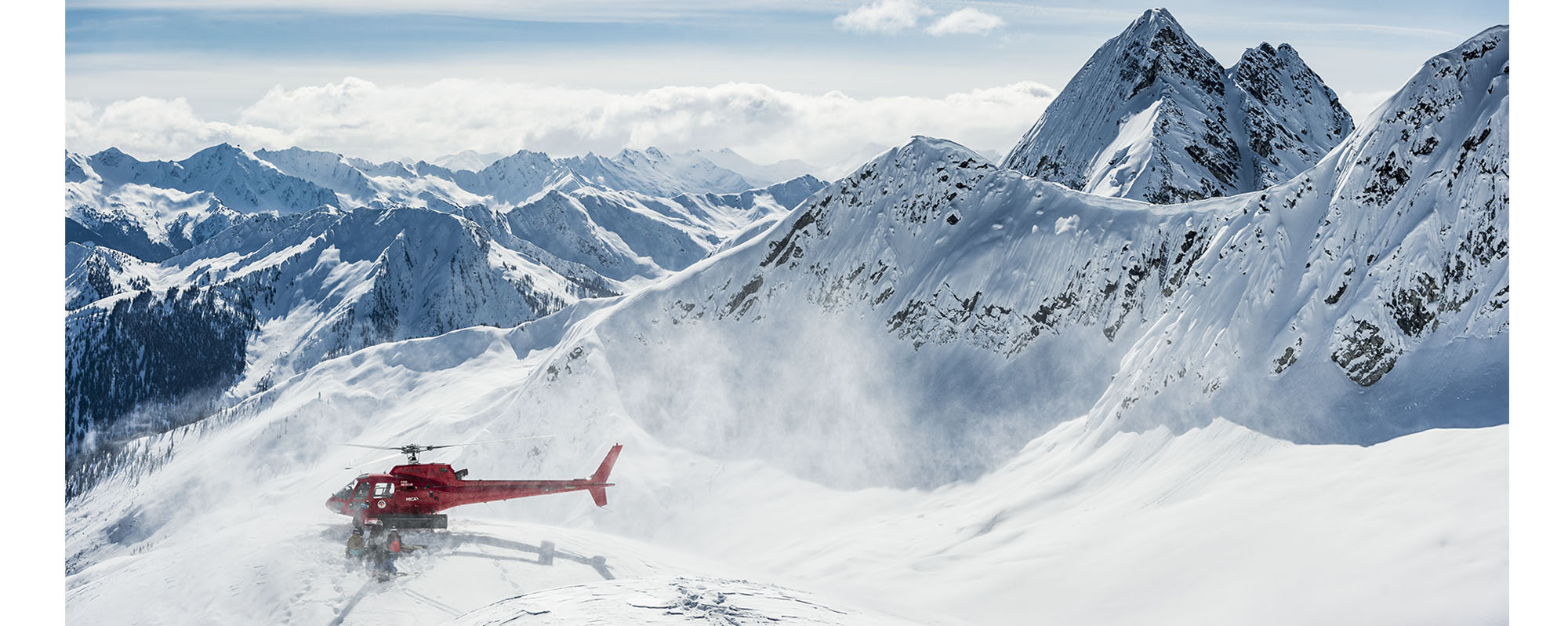 A red helicopter lands in a snowy mountain range in British Columbia