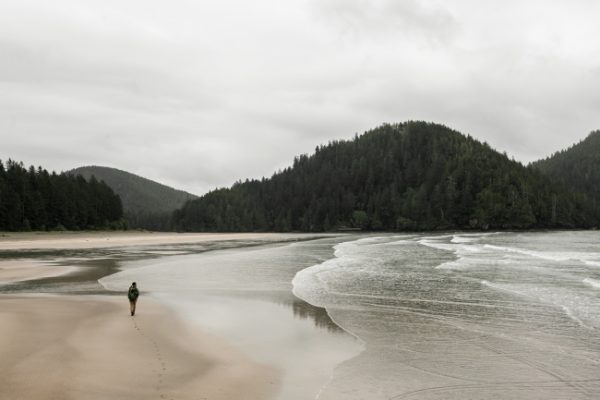 A man walks along the shore of the beach under an overcast sky.