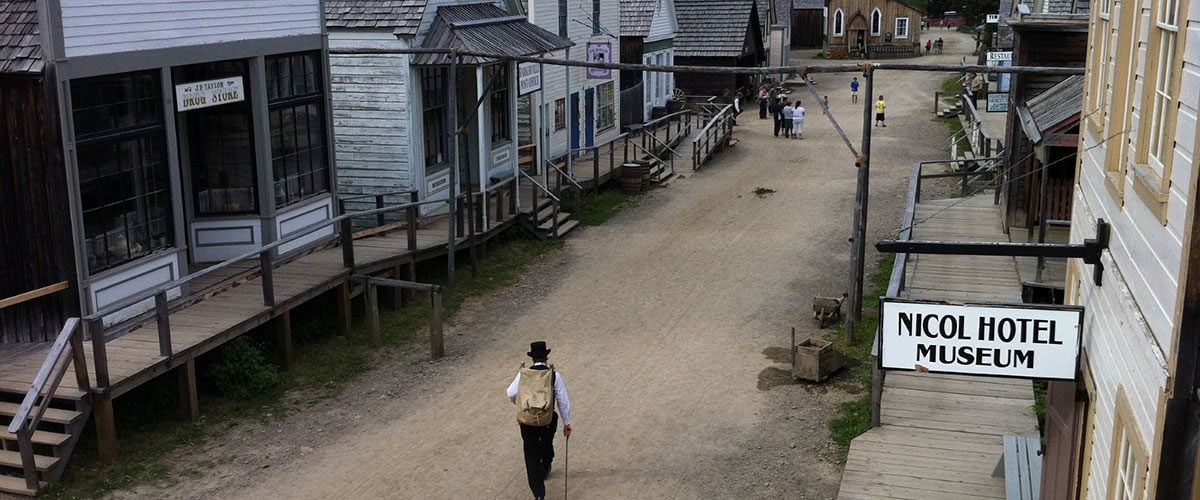 A person walks down a street in the historic town of Bakerville. There are historic wooden shops on both sides.
