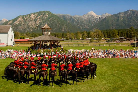 A large crowd sits and watches a circle of RCMP officers on horseback.