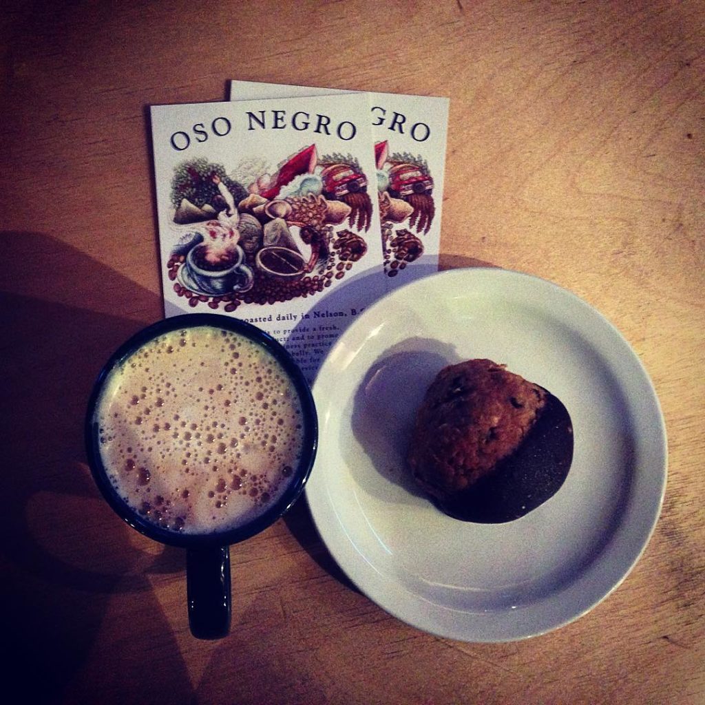 A mug filled with a foamy latte and a plate with a muffin on it.