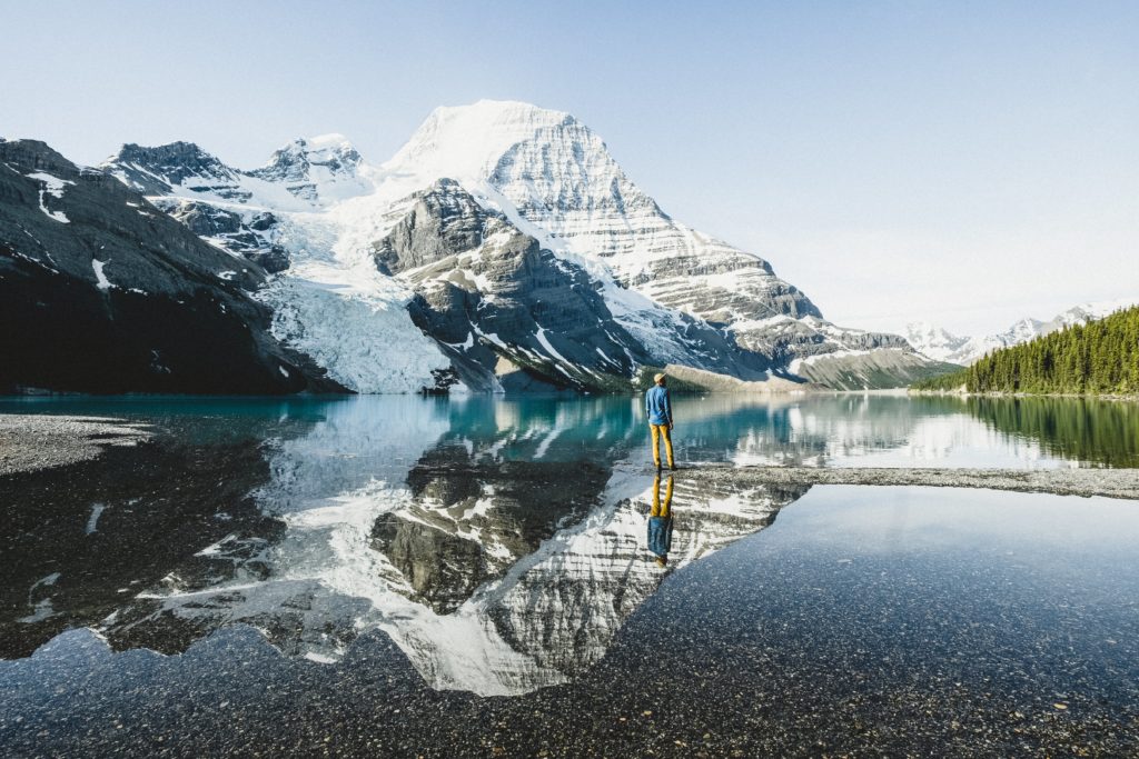 A man stops to take in the reflection of a snow-covered mountain in glassy waters.