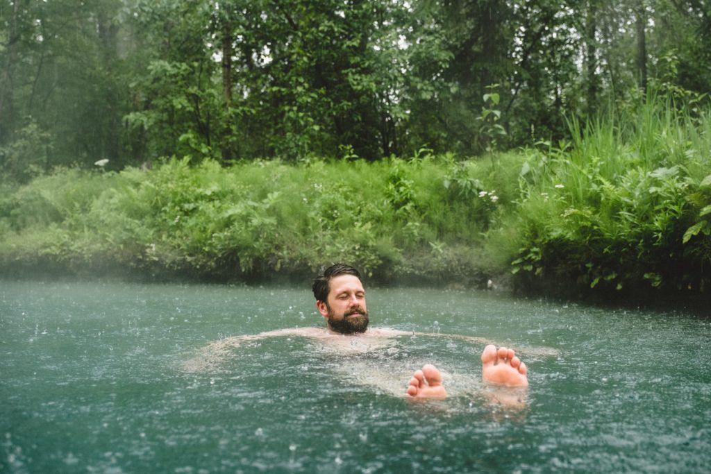 A man floats in a hot spring in the rain.
