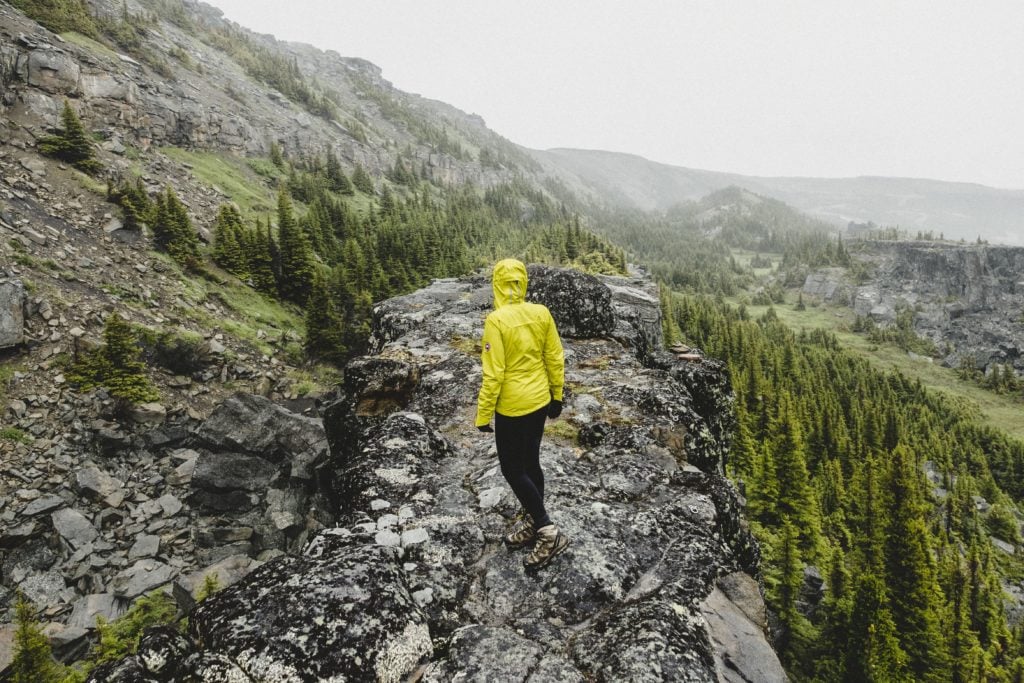 A woman in a yellow rain jacket hikes through a rocky landscape.