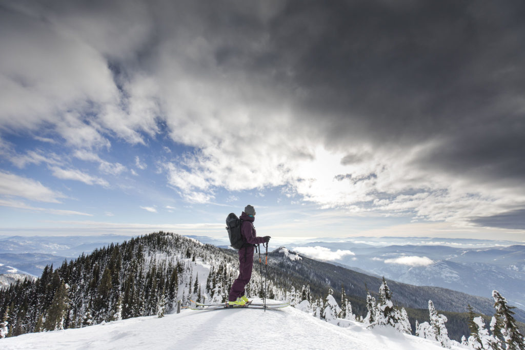 A single skier stands on top of a mountain peak at RED Mountain Resort