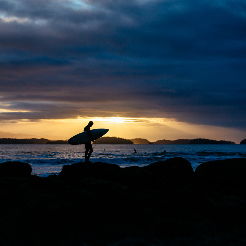 A silouette of @raphbruhwiler of Bruhwiler Surf School heading out for a sunrise surf with dark clouds and orange skies above by @jeremykoreski