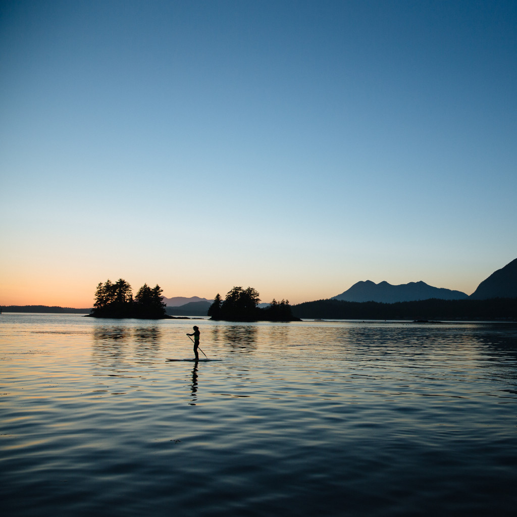 Silouette of @cathbruhwiler_tofinopaddlesurf enjoying an evening paddle on glass water with clear blue skies above in the Tofino Harbour by @jeremykoreski