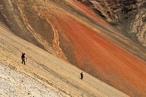 Two hikers using walking poles as they hike into the orange core of Rainbow Volcano.