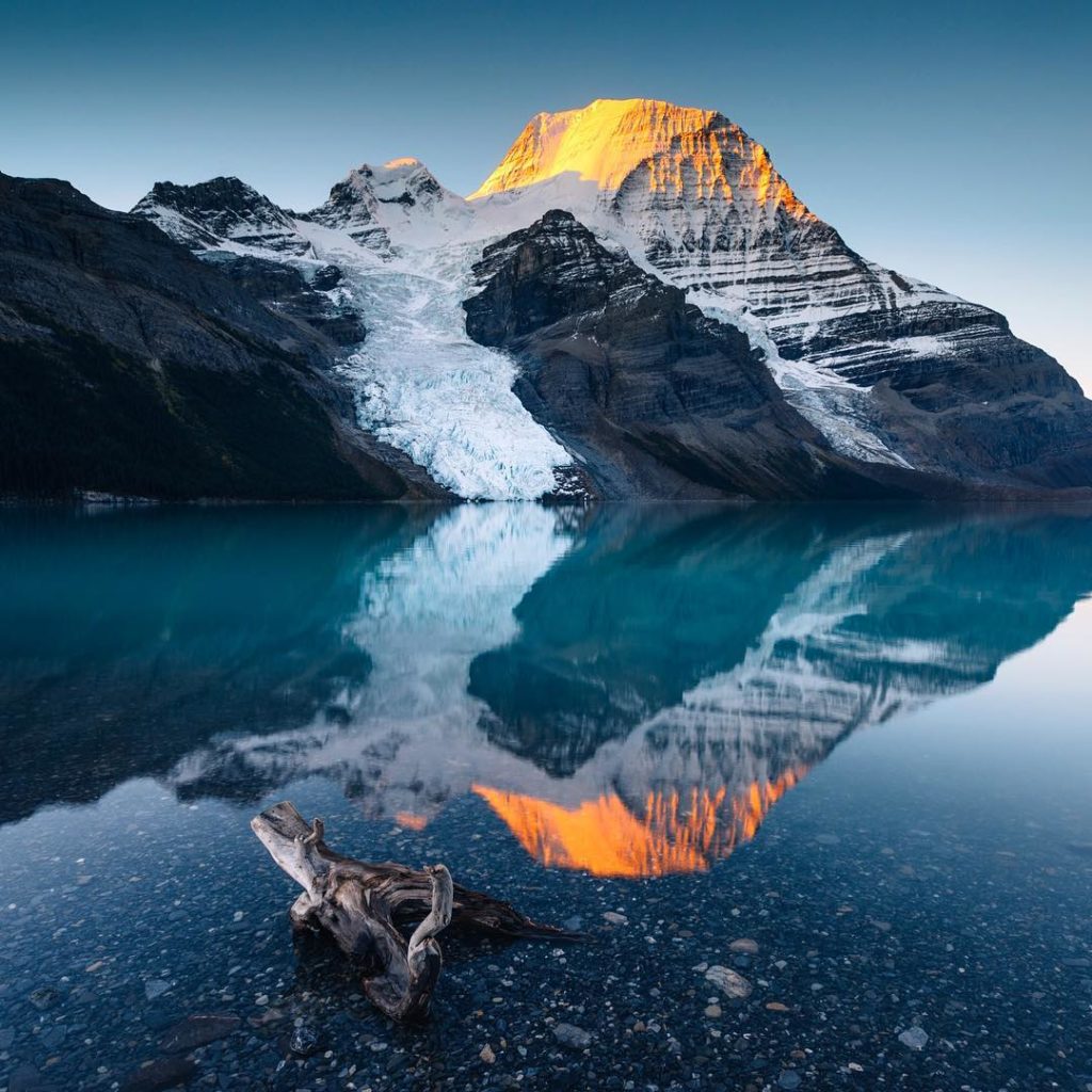 Placid waters reflect glacial mountains at sunset.
