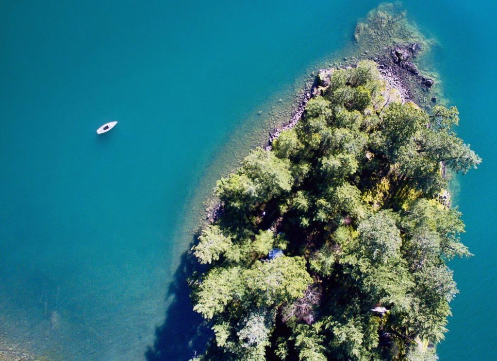 Aerial view of a densely forested island surrounded by emerald blue water.