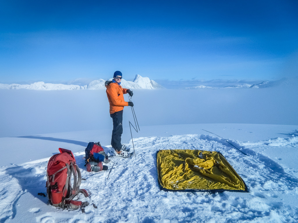 A man takes down a yellow tent in a snow-covered landscape.