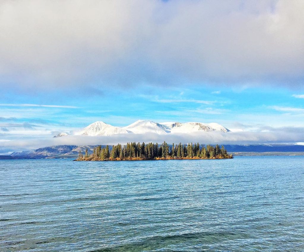 An densely forested island with snow-capped mountains rising behind it.