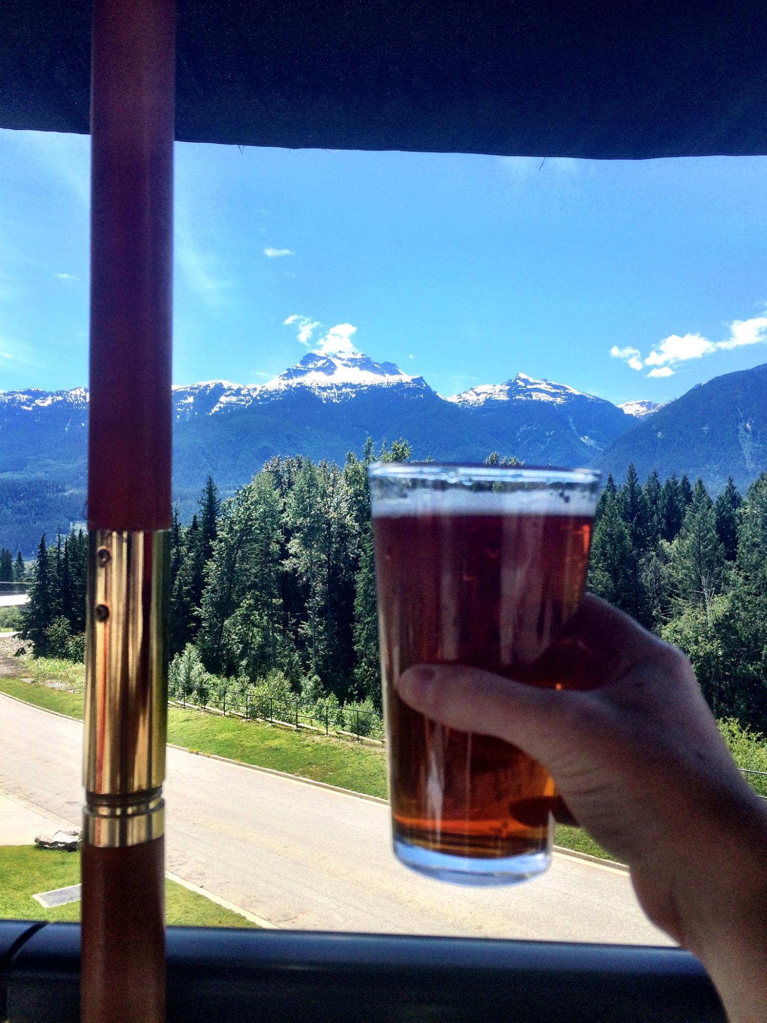 A hand holds up a full pint glass in front of a mountainous landscape.