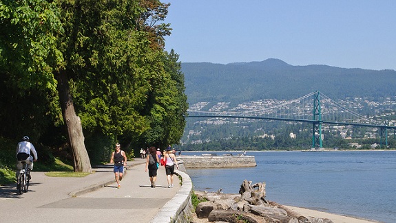 Groups of people walk, jog, and bike along the Stanley park Seawall.