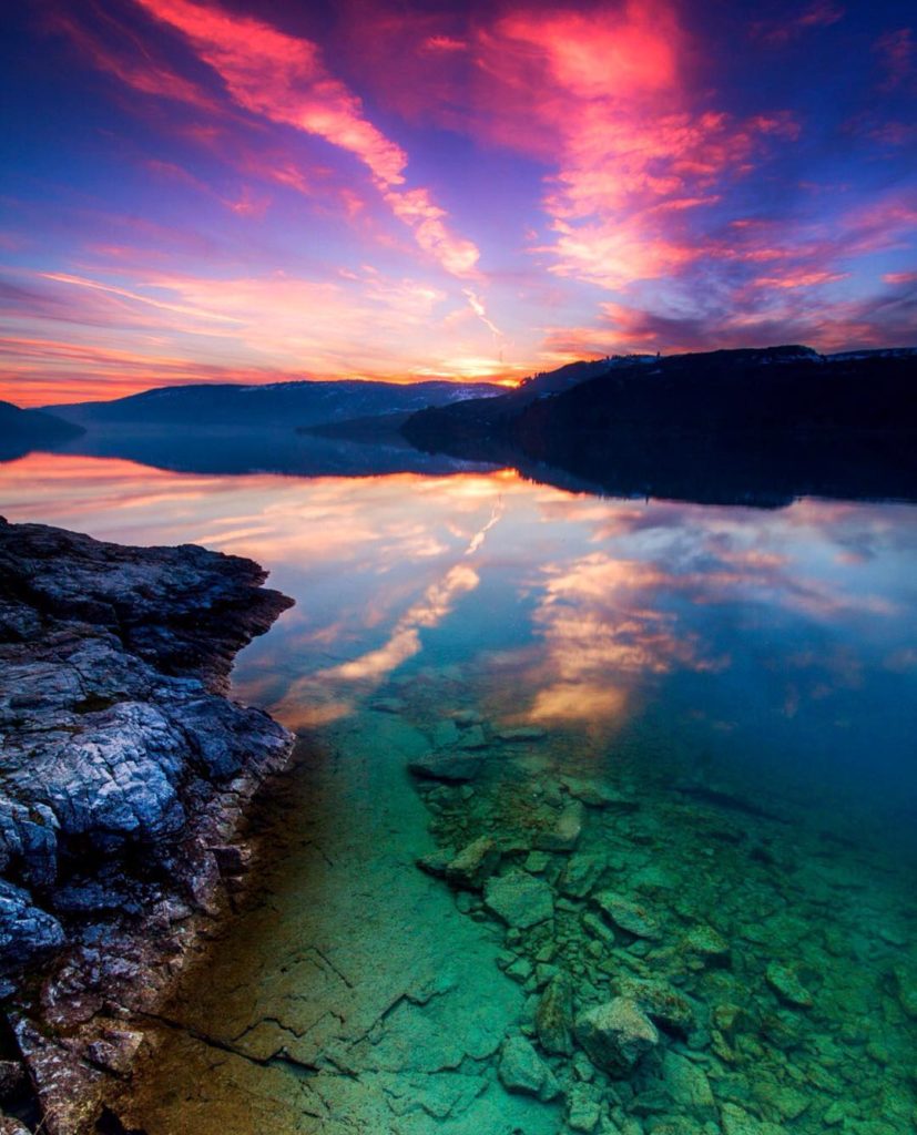 A multicolored sunset is reflected in a glass-like lake.