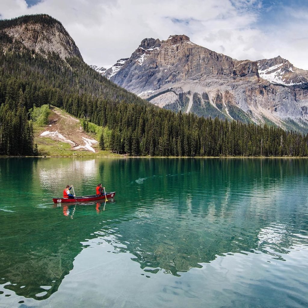 Canoeing through Emerald Lake, lined with dense vegetation and snow-capped mountains. 