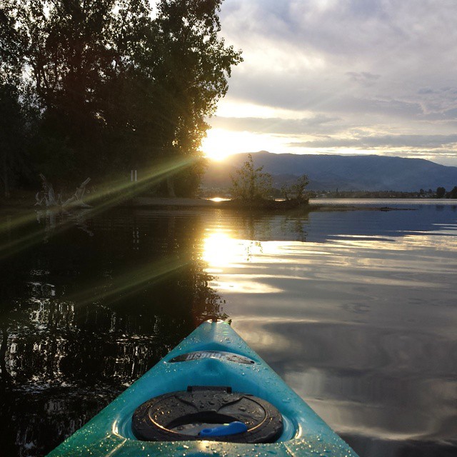 A kayak travels through quiet waters at sunset.