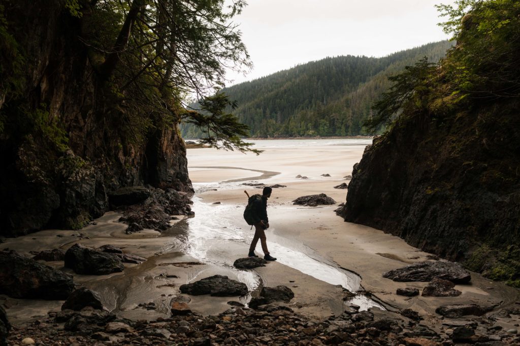A man explores a rocky coastline and a sandy beach.