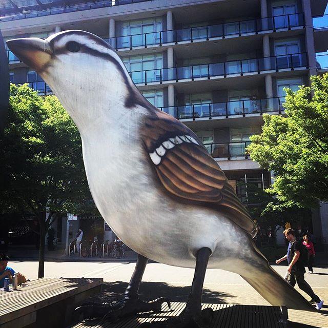 People stroll past a statue of a giant sparrow.