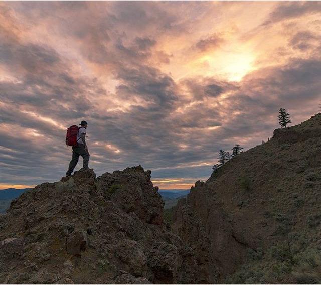 A man hikes a rocky landscape at sunset.
