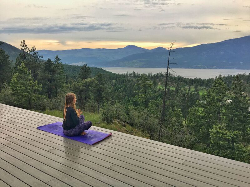 A young girl practices yoga outdoors with views of the mountains.