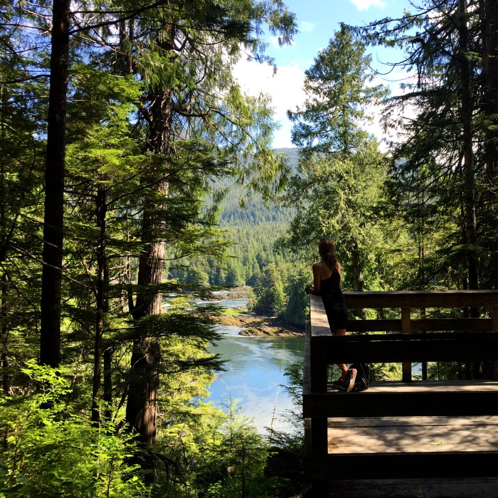 A female hiker standing on a boardwalk looking out at the trees and water from the Butze Rapids trail near Prince Rupert.