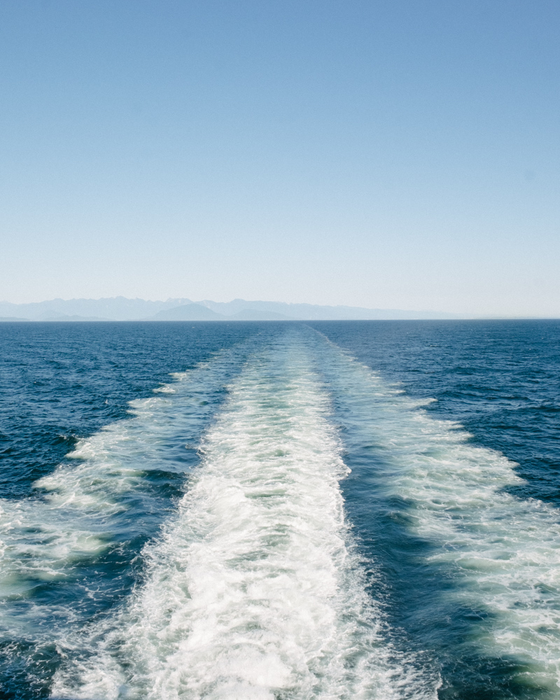 A wave behind a ferry boat in the open ocean. Mountains are seen in the fast distance. 