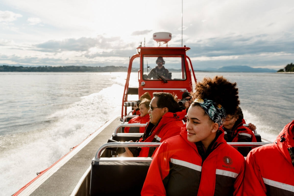 People wearing red jackets are in a whale watching boat on the water. 