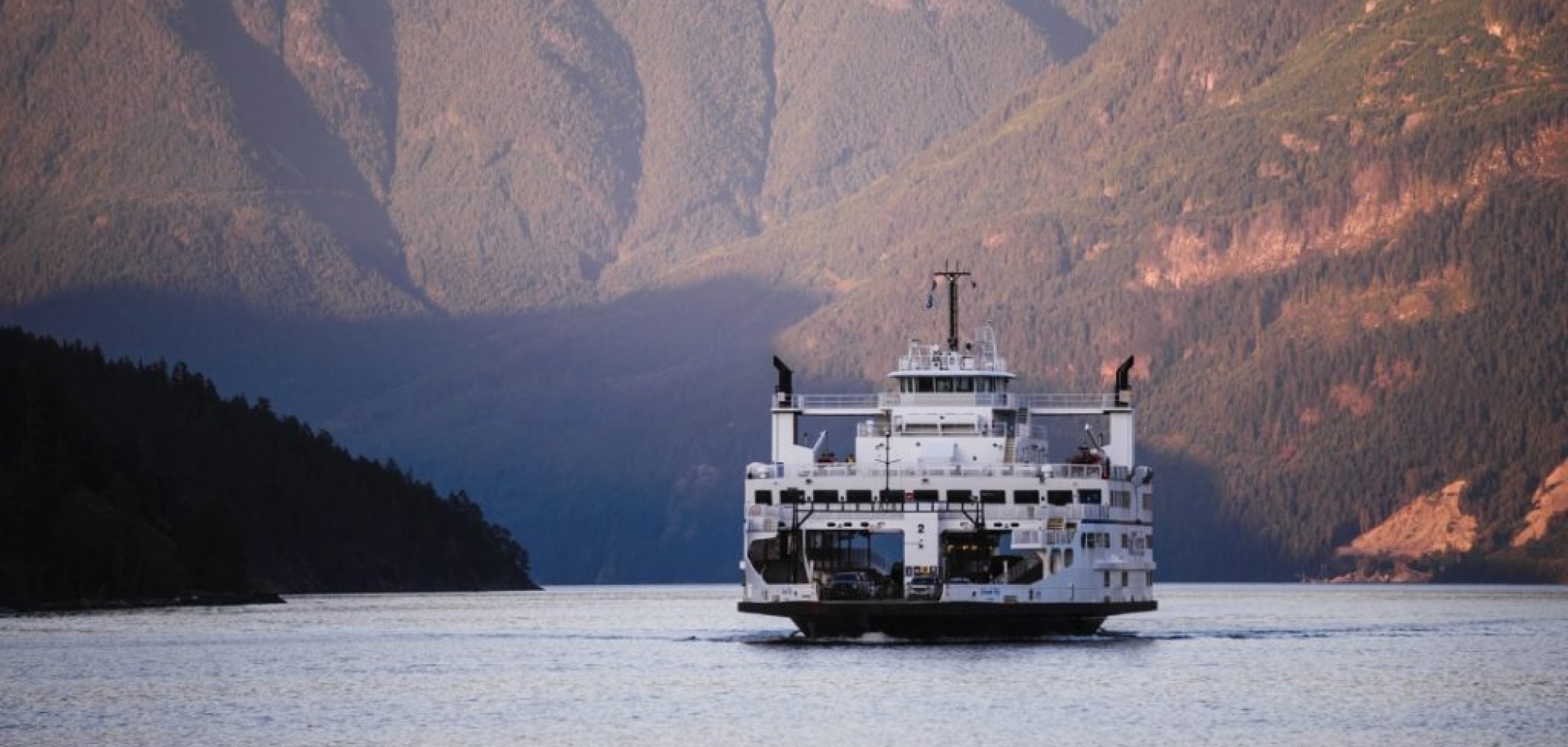 A ferry on the water in front of large mountains behind it