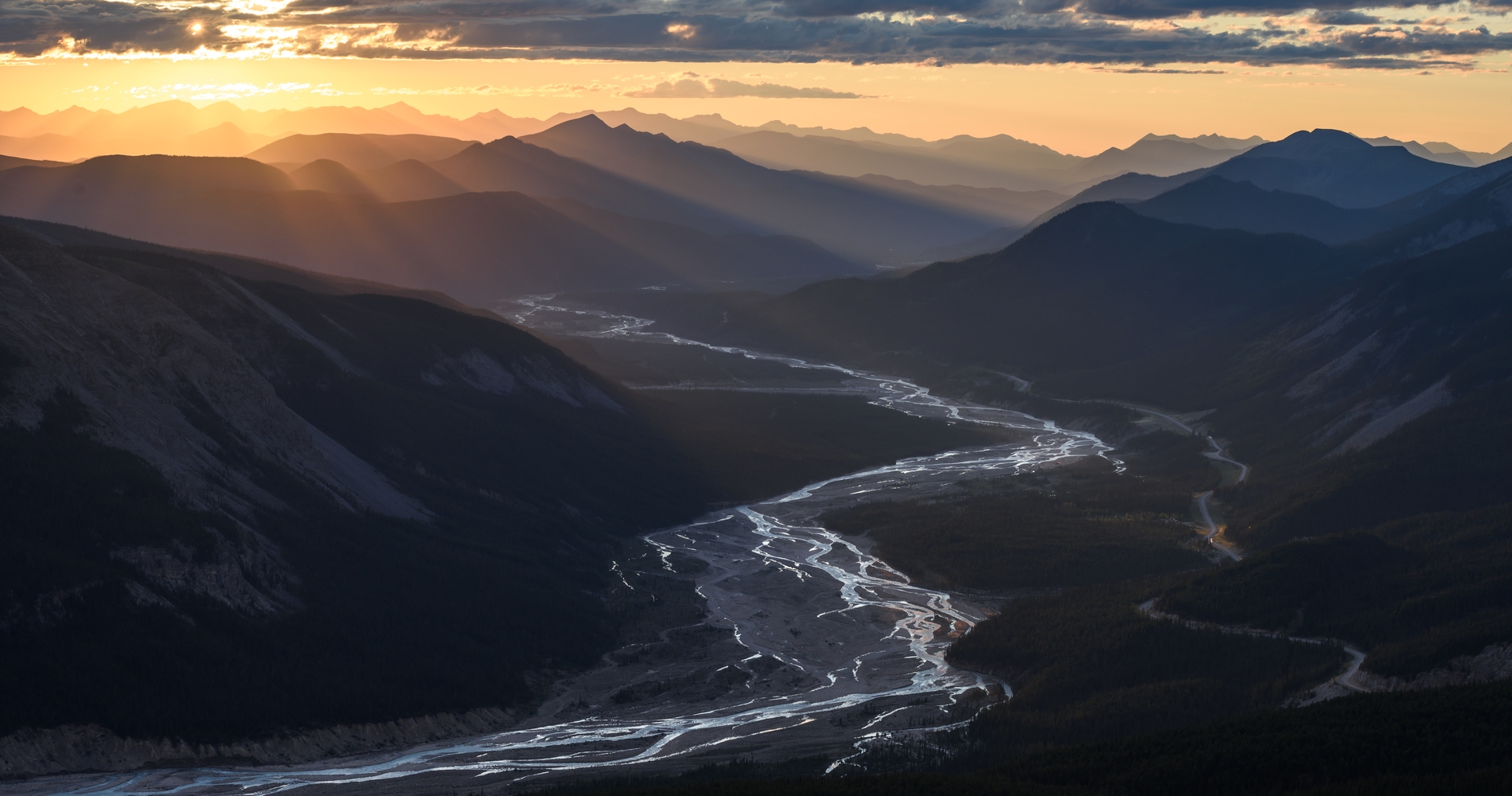 A meandering series of river streams run through a valley at sunset surrounded by mountains