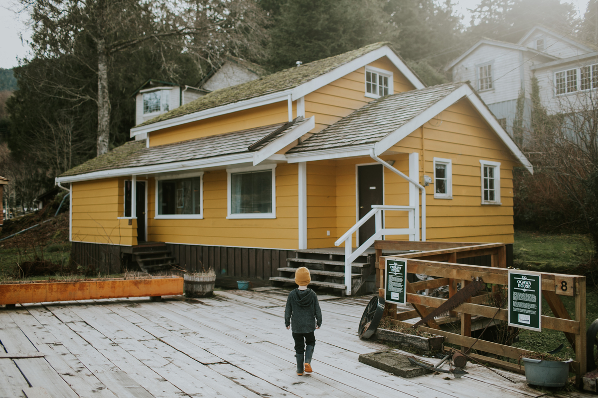 A yellow building sits on the wooden boardwalk at Telegraph Cove Resort as a small child walks toward the building