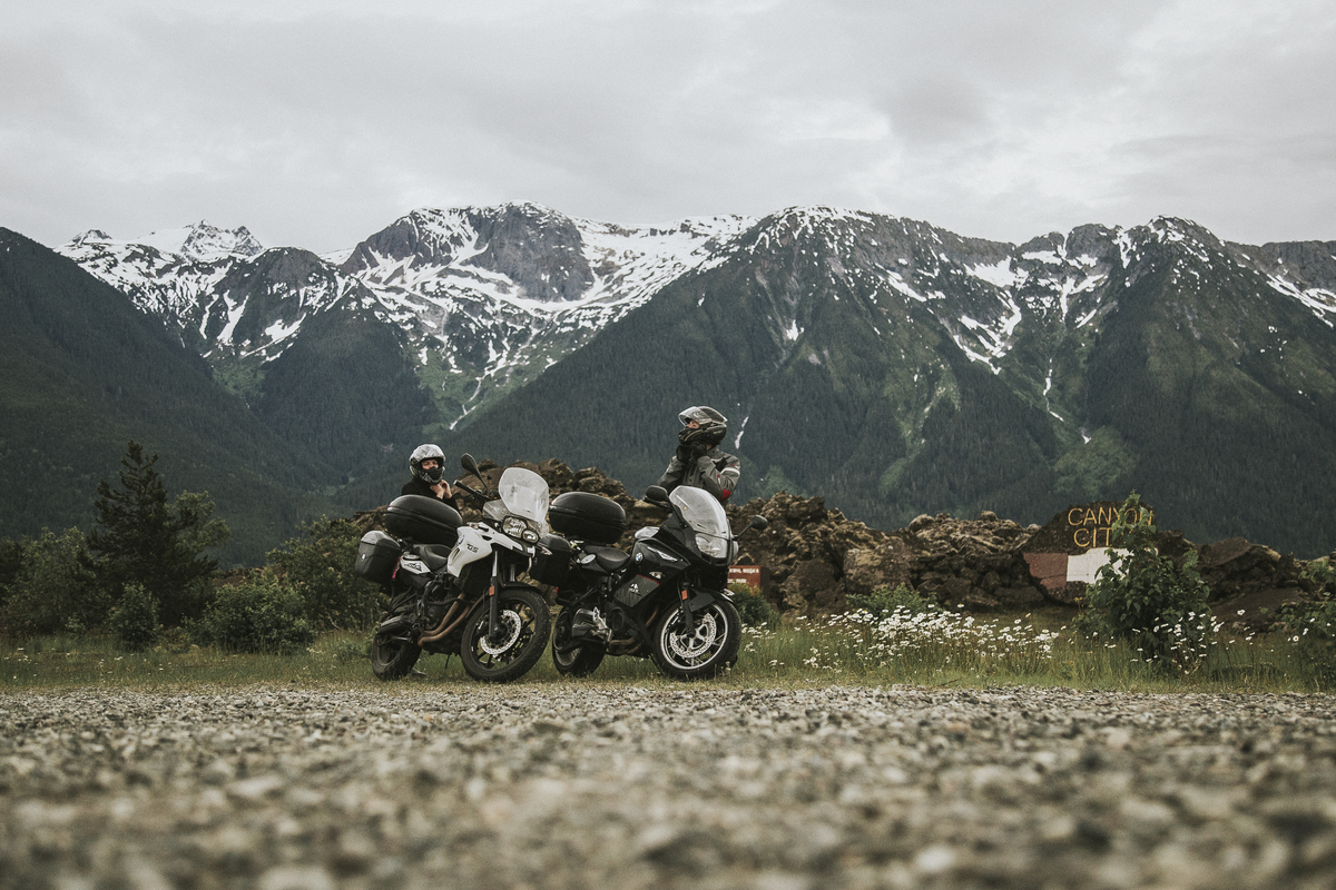 Two riders dismount their motorcycles parked overlooking a mountain range